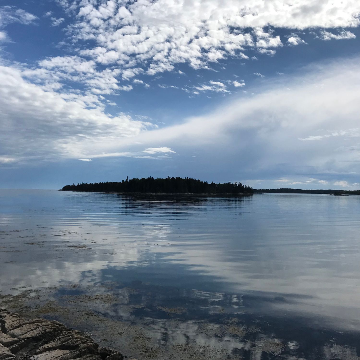 Peaceful coastal landscape photo with an island and scattered clouds reflected in still waters used as a reference for a landscape painting.