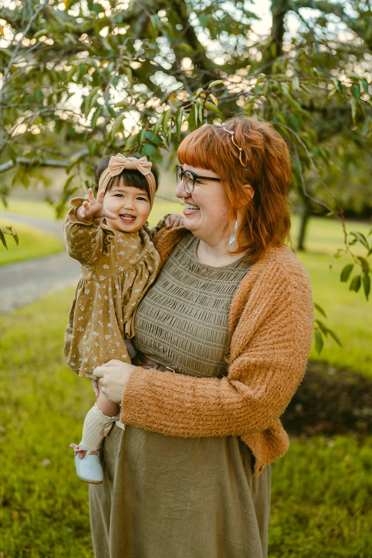 A mother holding her child laughing with a tree and grass in the background at Cornwall Park, Auckland.