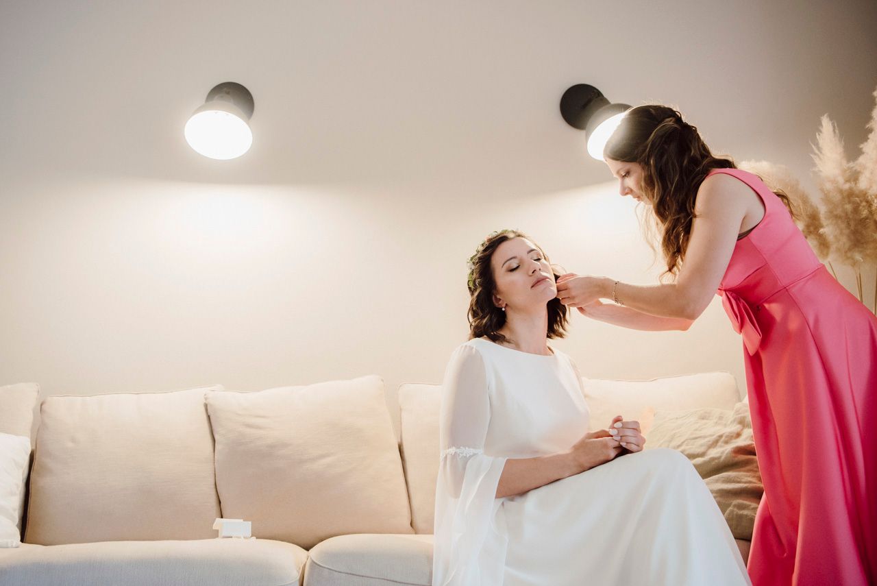 Applicazione di trucco professionale su una sposa vestita di bianco e seduta su un divano chiaro con illuminazione interna.