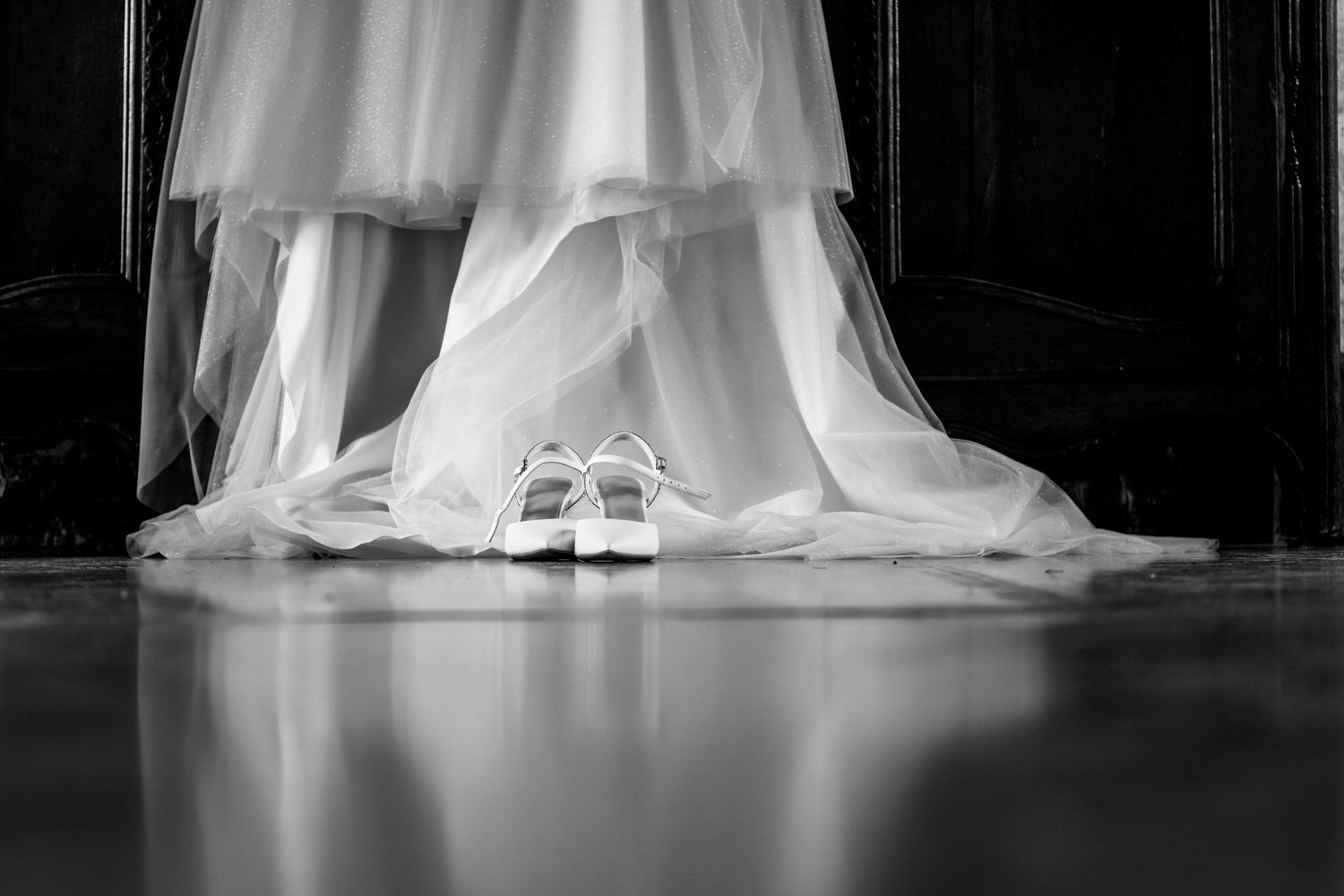 Eleganti scarpe da sposa bianche si trovano sotto strati fluenti di un abito da sposa in bianco e nero.