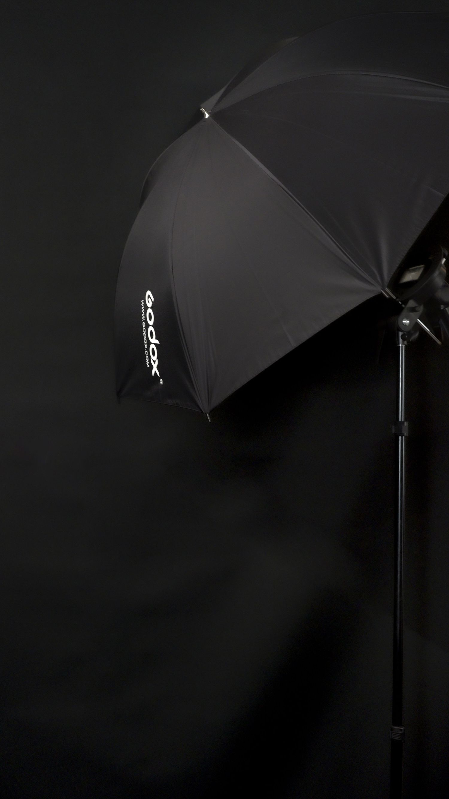 A series of black umbrellas mounted on photography light stands against a dark background create dramatic studio lighting.