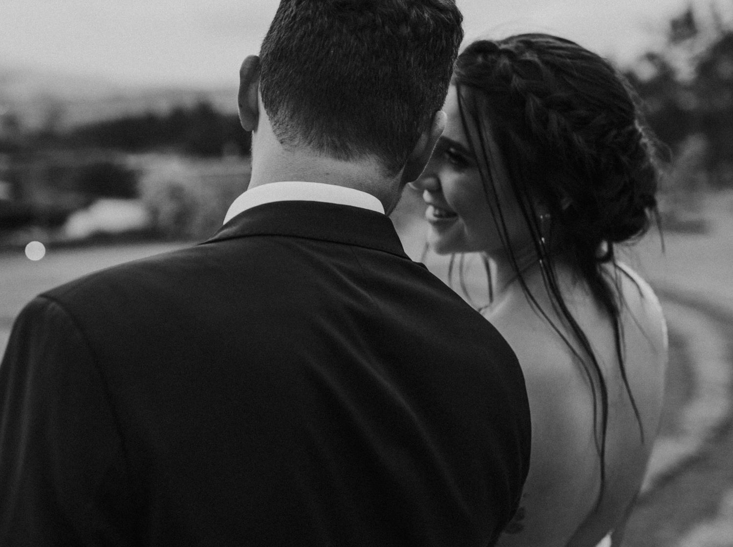 Intimate black and white close-up of bride smiling as she leans toward her groom outdoors.