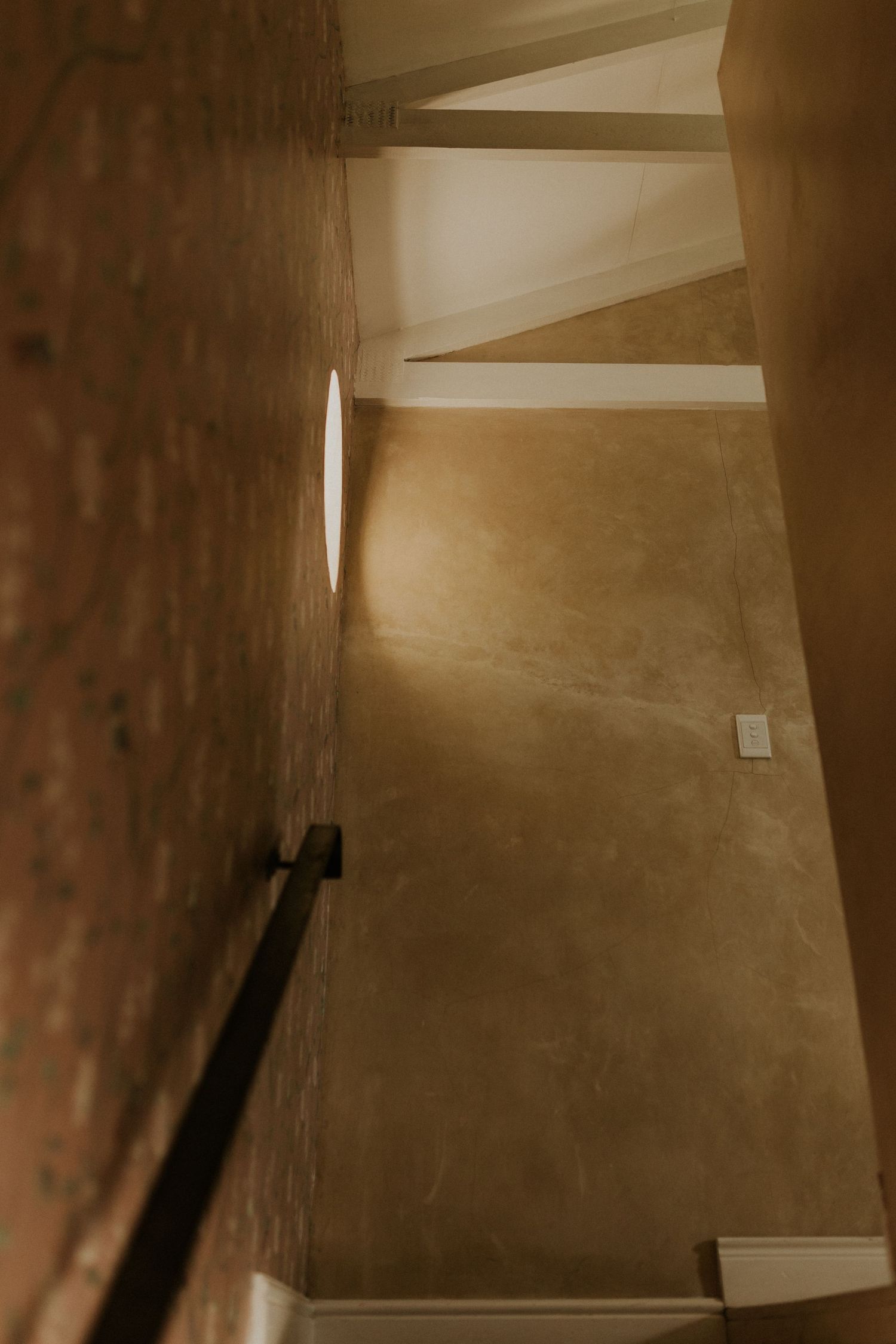 Dimly lit stairwell with warm golden walls, a handrail, and a circular wall sconce casting soft light.