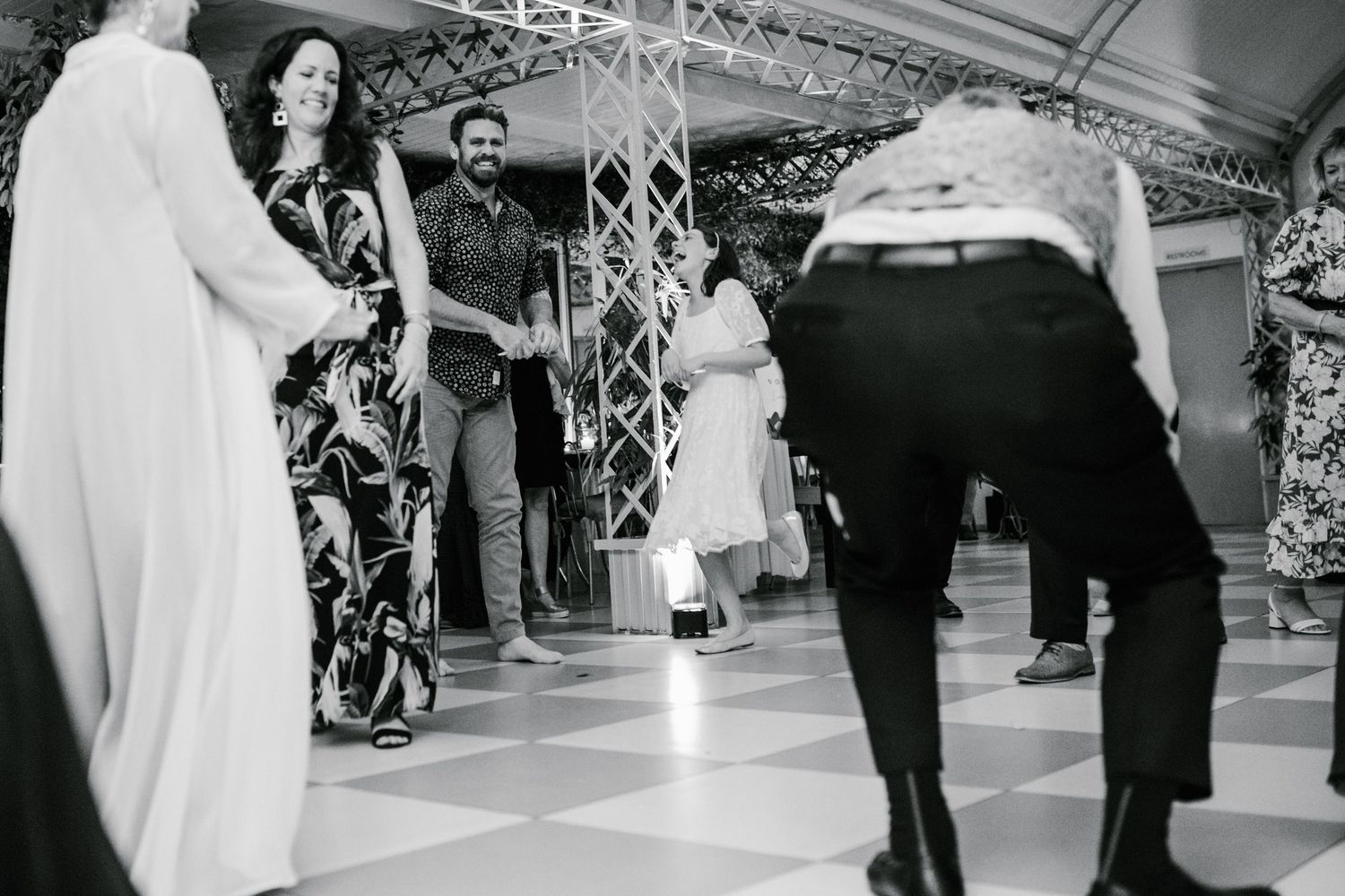 Wedding guests watching someone perform dance moves on checkered ballroom floor.