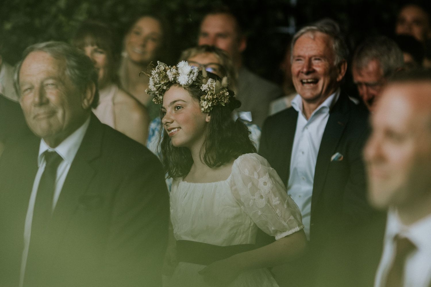 Smiling bride wearing a floral crown laughs joyfully among wedding guests during the celebration.