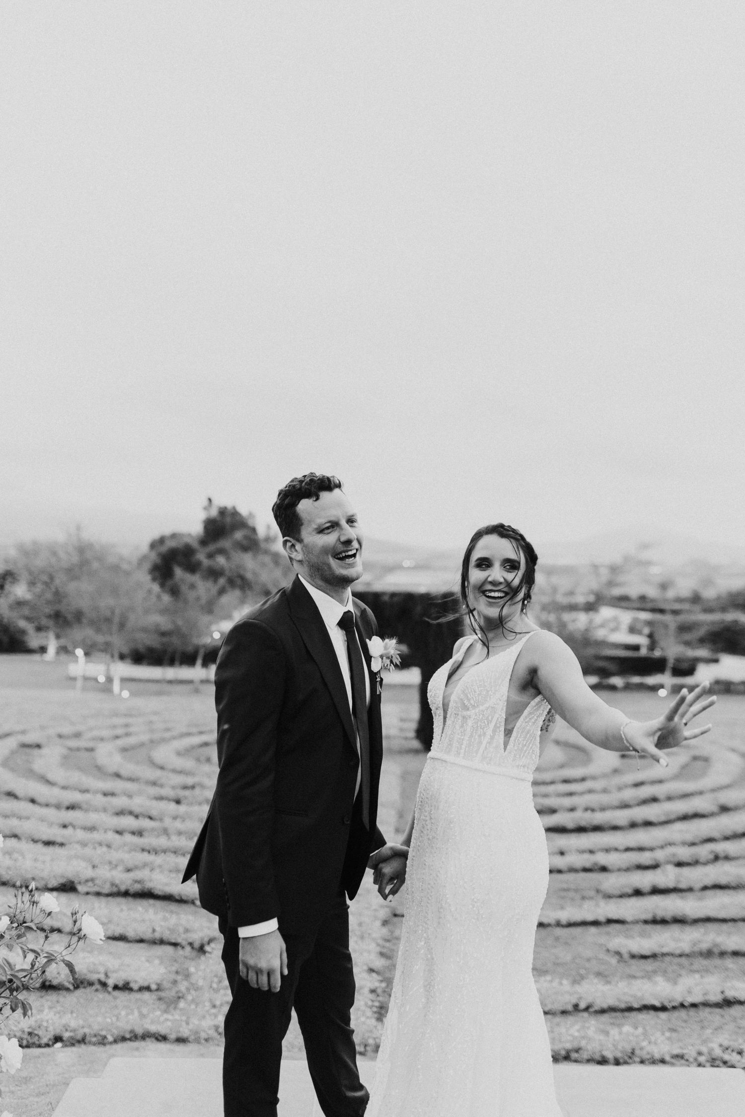 Joyful bride and groom holding hands laughing in black and white wedding portrait outdoors.