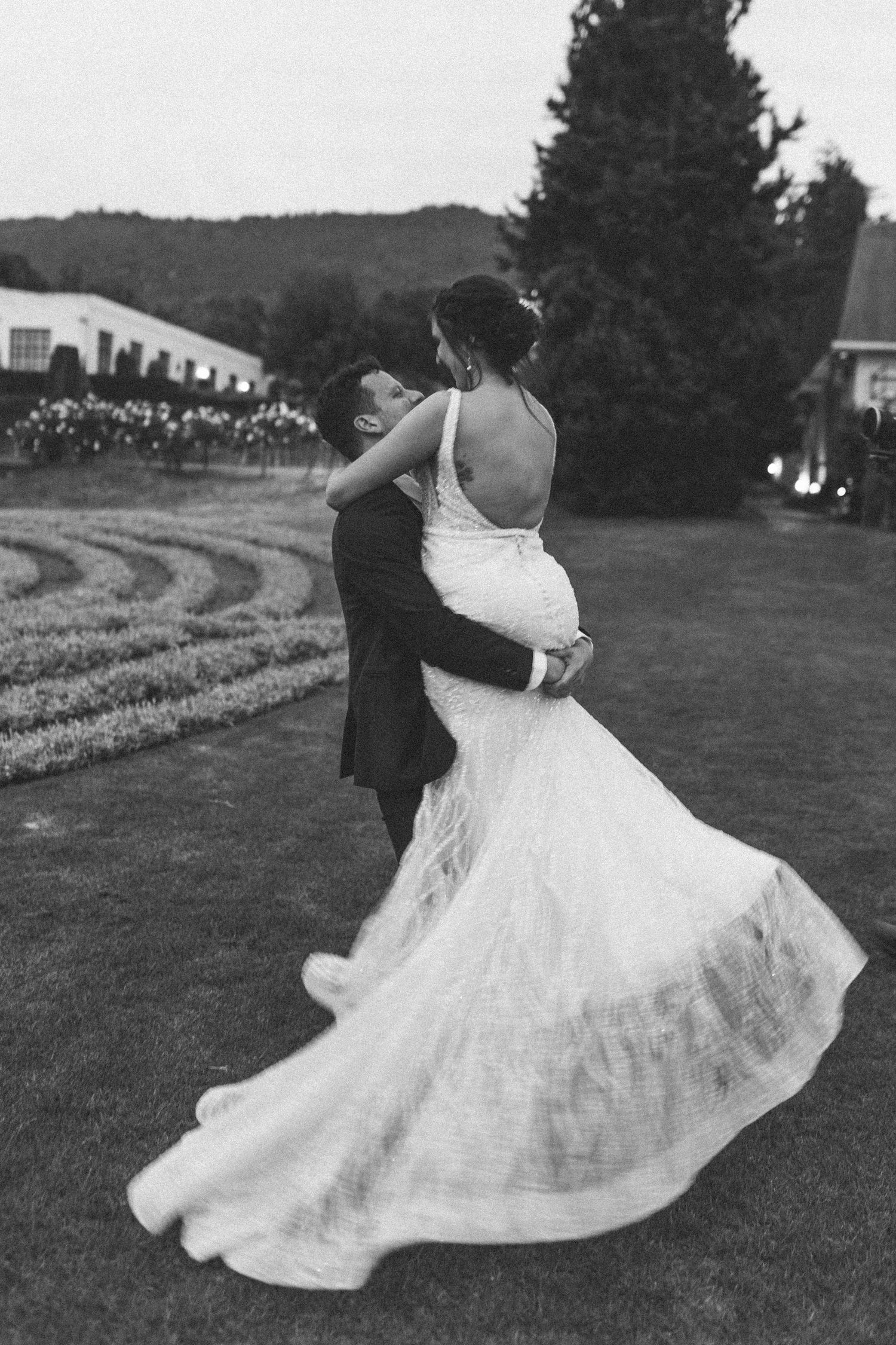 Groom lifts bride in flowing lace gown in romantic black and white outdoor wedding photo.