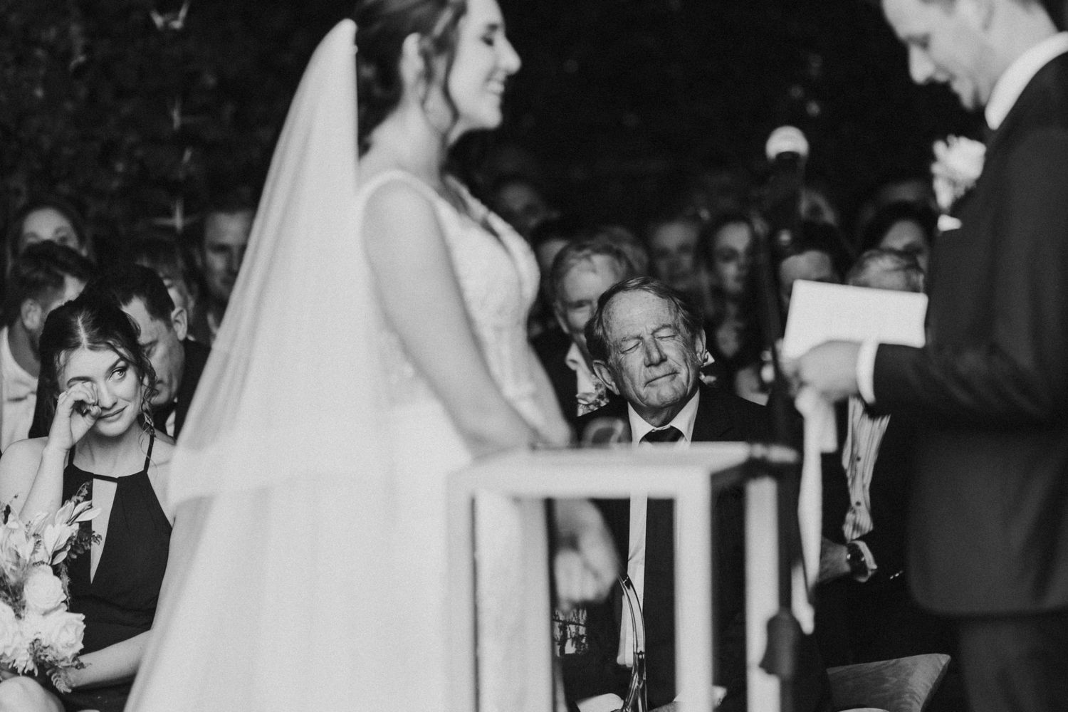 Black and white photo of emotional wedding guest wiping tears during heartfelt outdoor ceremony.