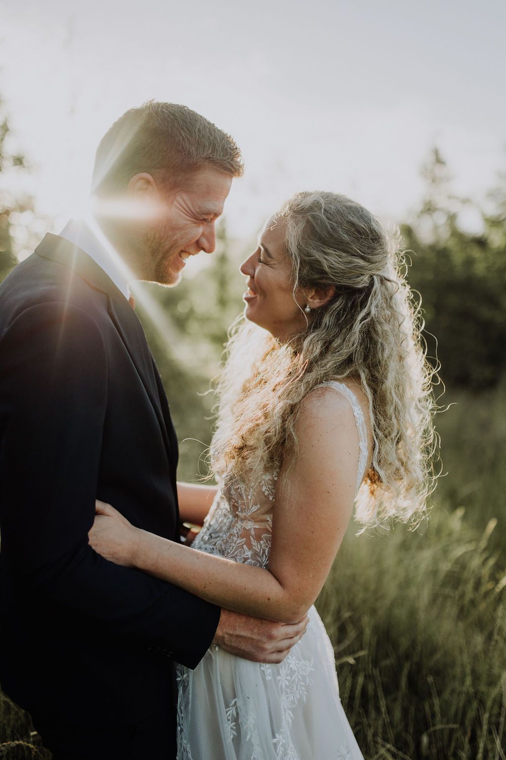 Laughing bride and groom embracing in a sunlit field, radiating joy on their wedding day.