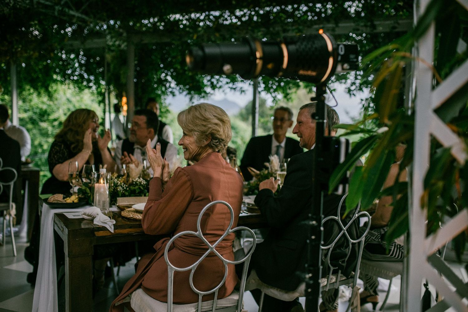 Wedding guests dining under a lush green pergola with candlelit tables at an elegant outdoor reception.