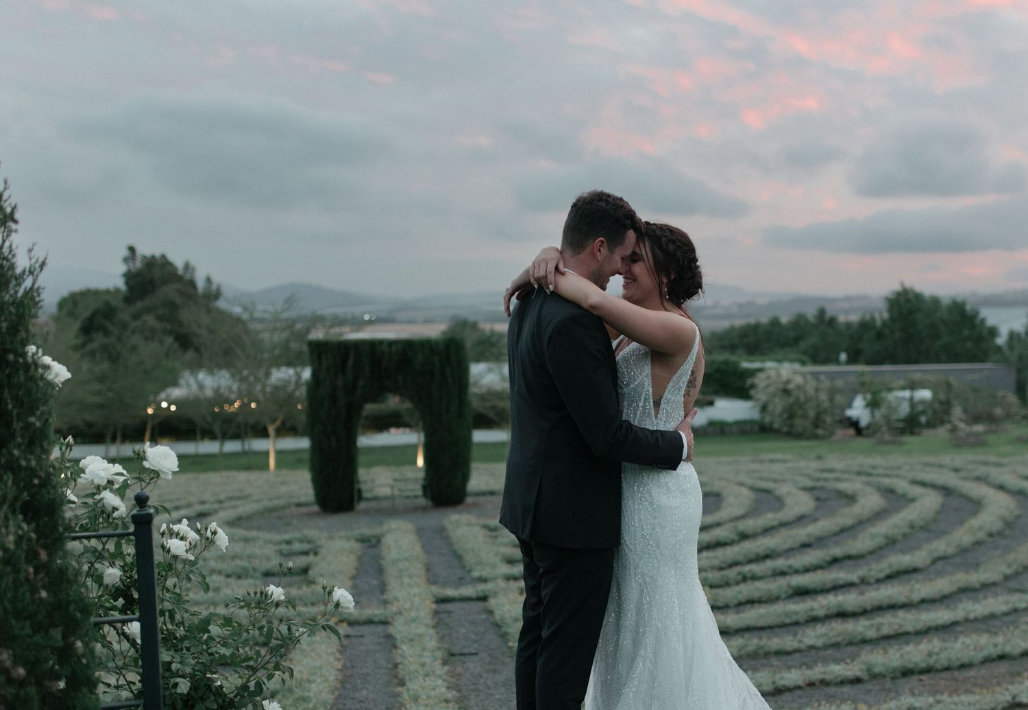 Bride and groom sharing a romantic embrace at sunset in a beautiful garden wedding venue.