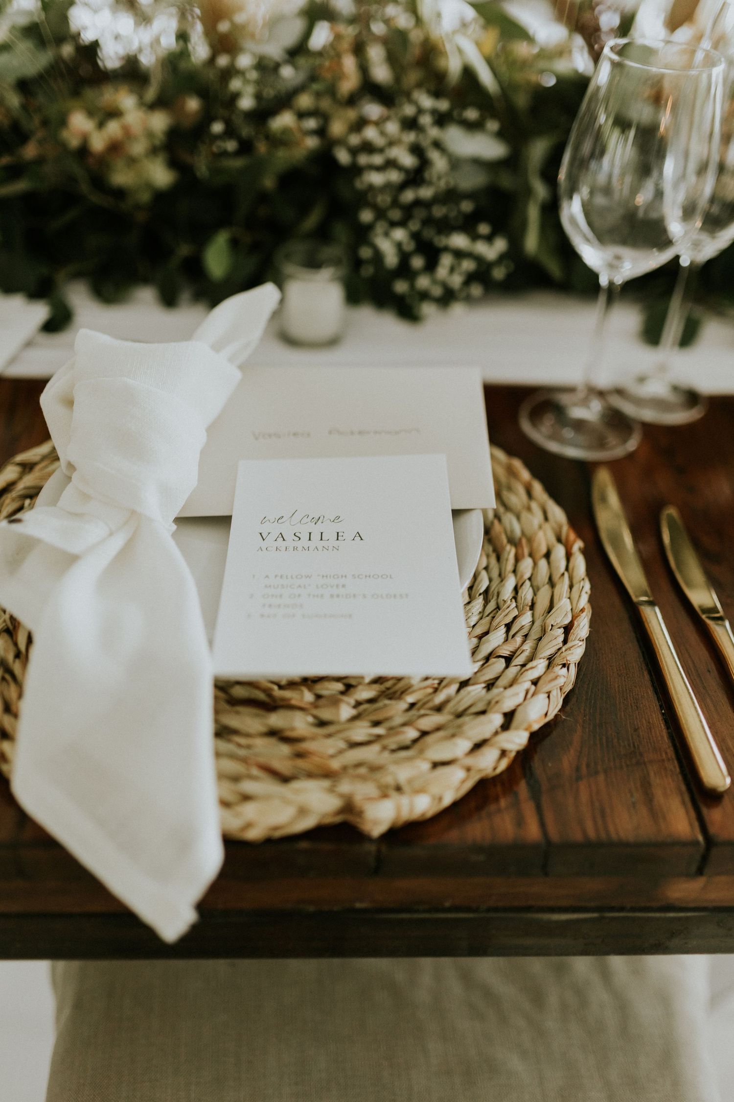 Elegant wedding place setting with woven charger plate, white linen napkin, gold cutlery, and personalized menu card.