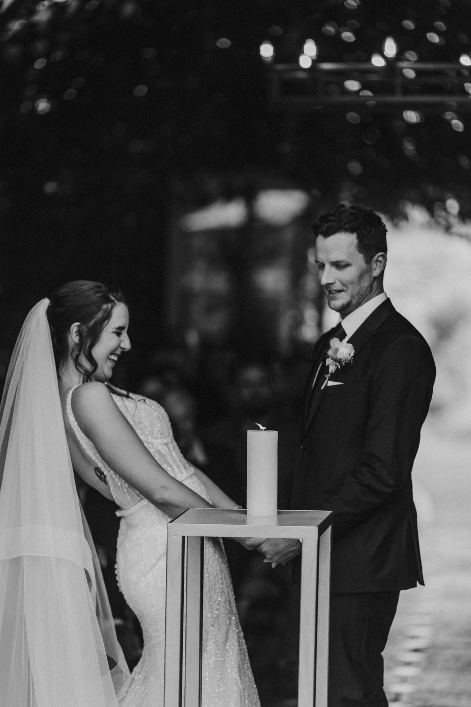 Bride and groom smiling together at unity candle during elegant outdoor wedding ceremony.