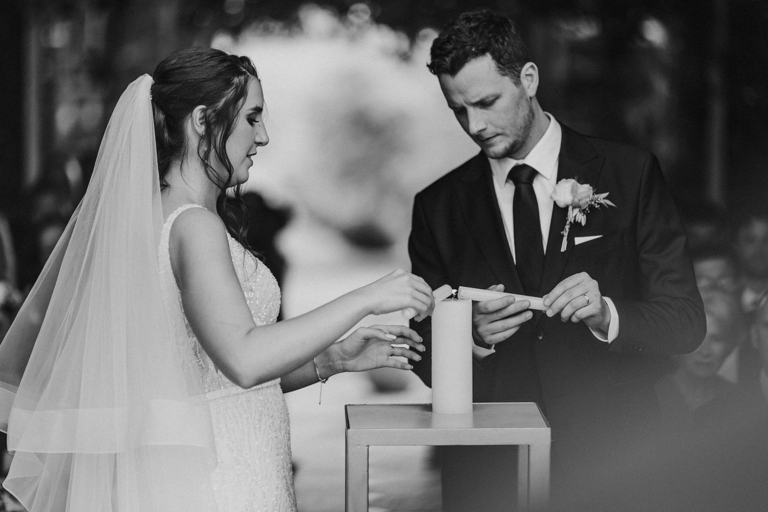 Bride and groom lighting unity candle together during black and white wedding ceremony.