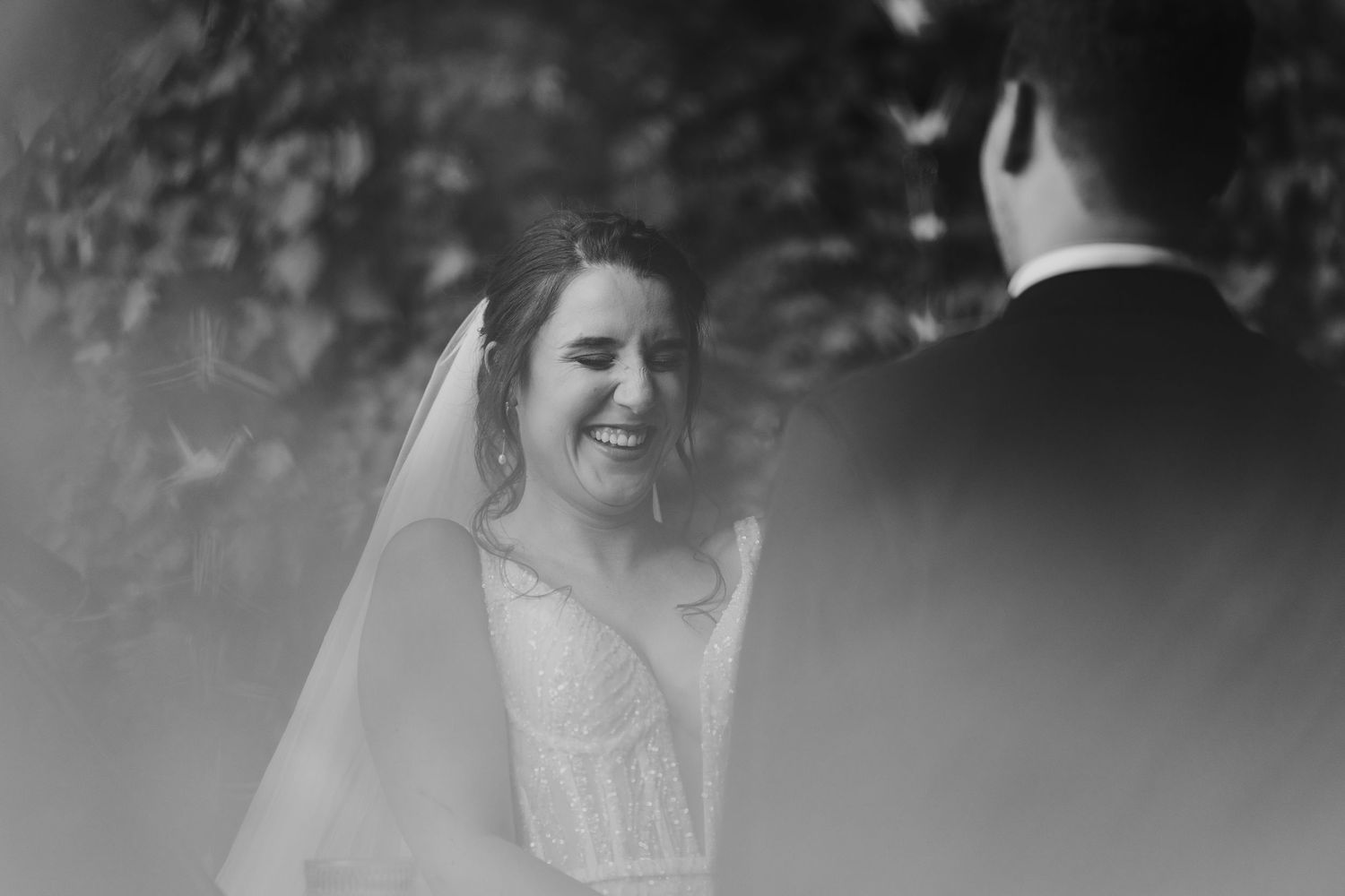 Black and white photo of a radiant bride laughing happily during her outdoor wedding ceremony.