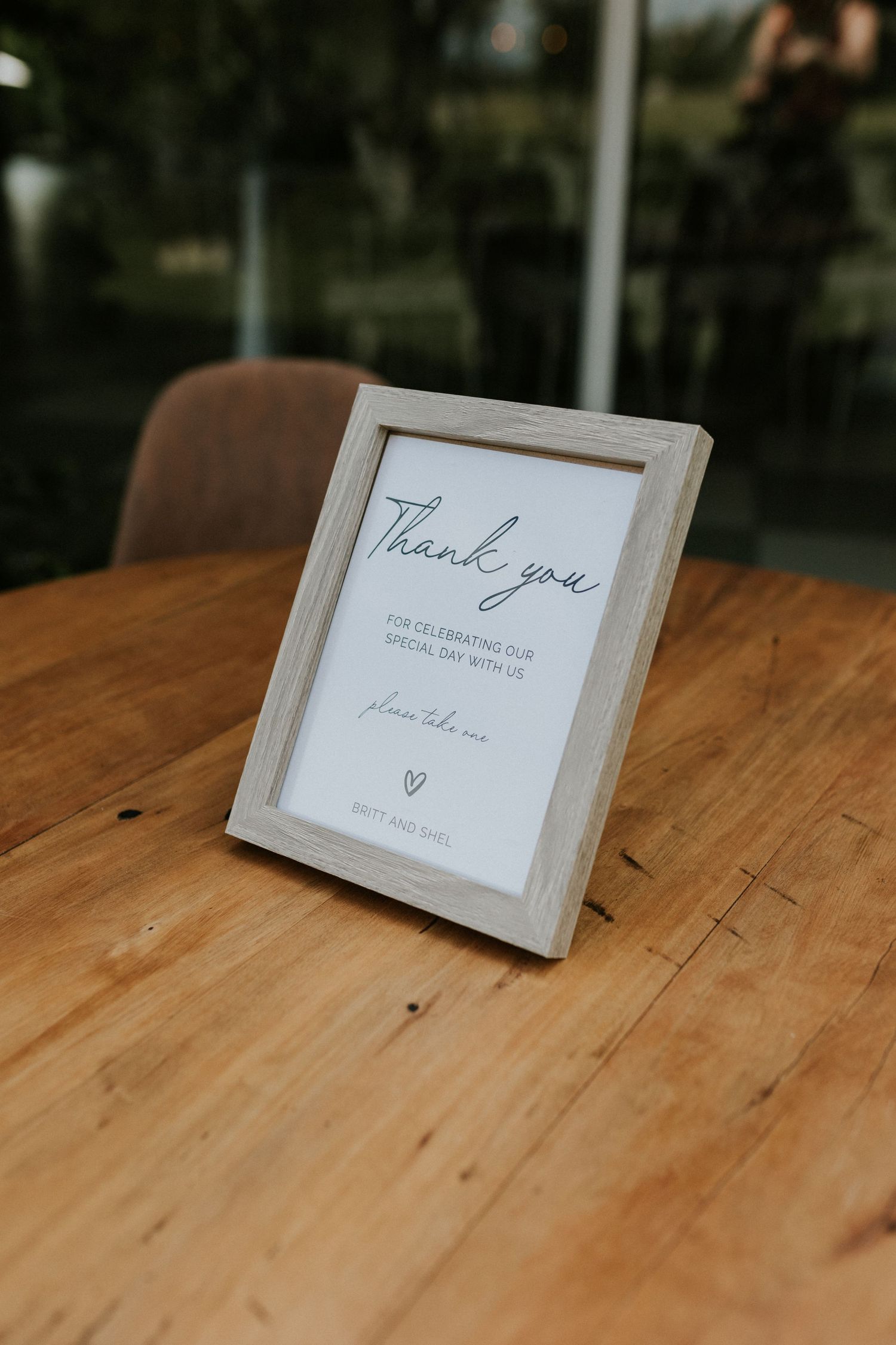 Elegant wooden framed thank you wedding sign on a rustic wooden table with lush greenery in background.