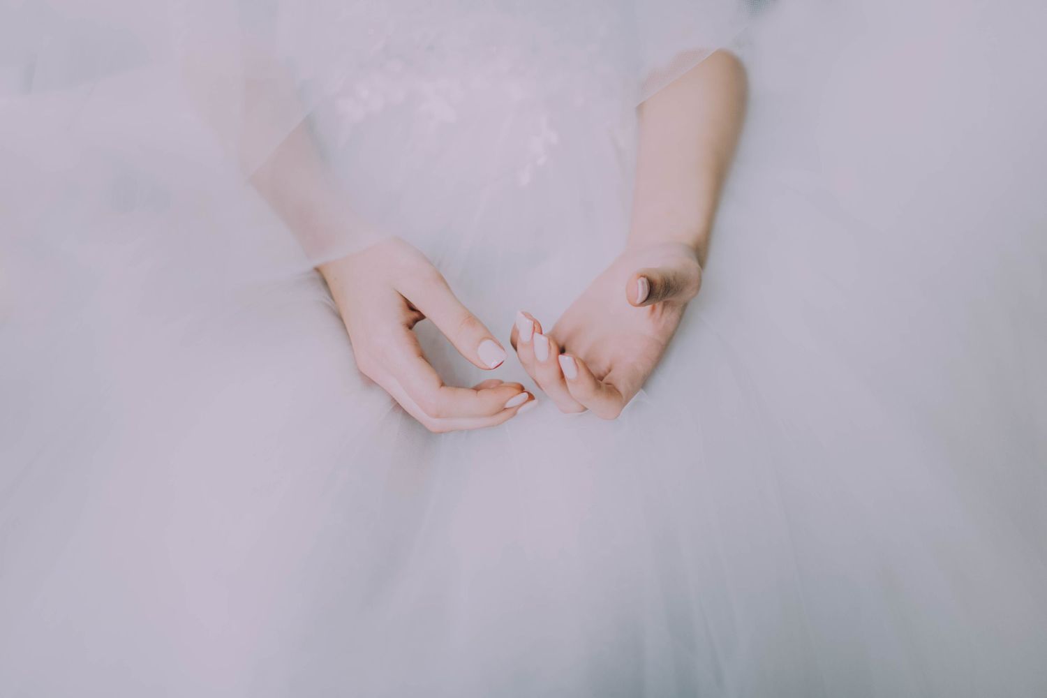 Close-up of bride's hands clasped together in white tulle wedding dress.