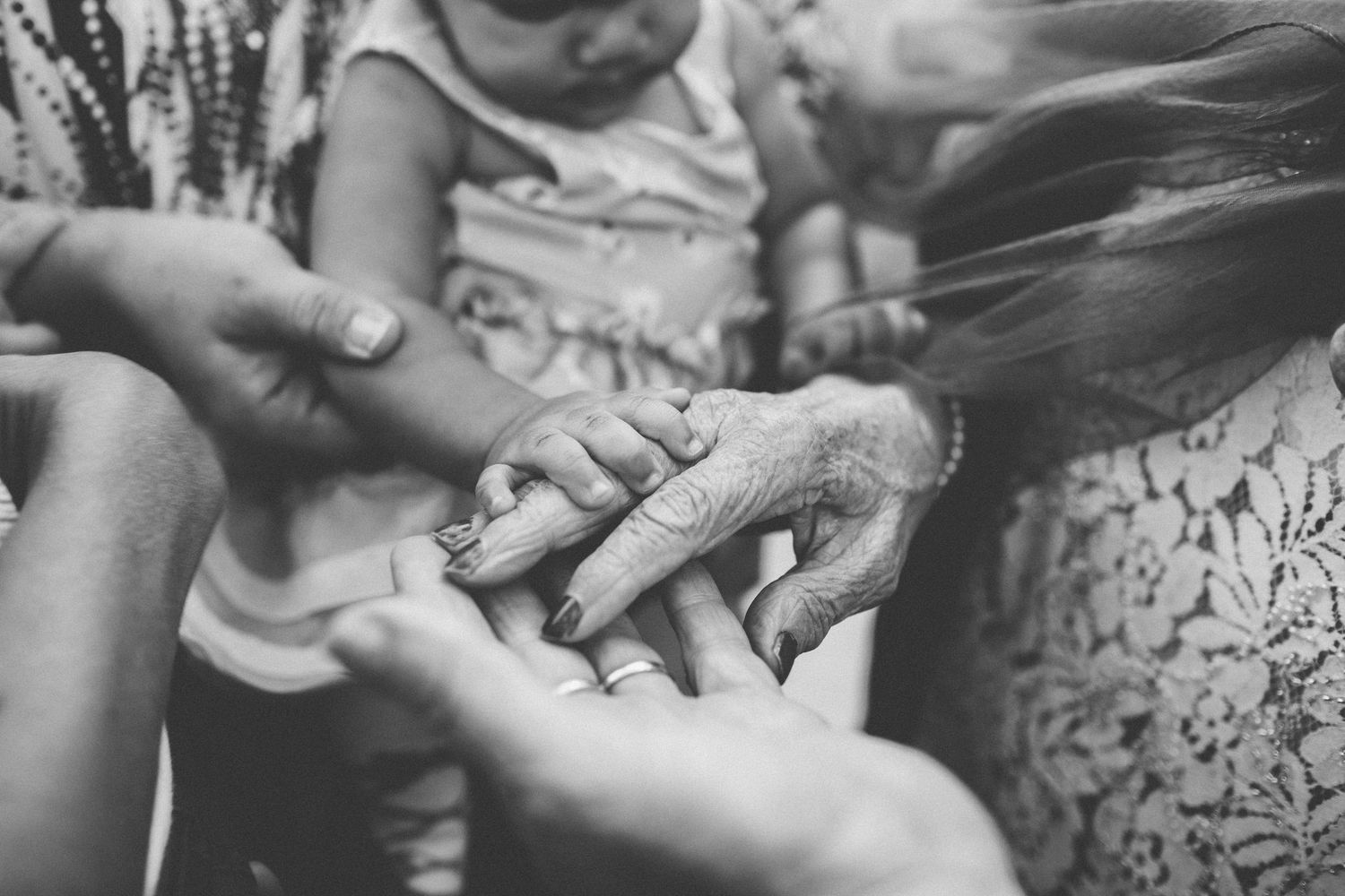 Black and white close-up of a newborn baby hand resting on elderly and adult hands across generations.