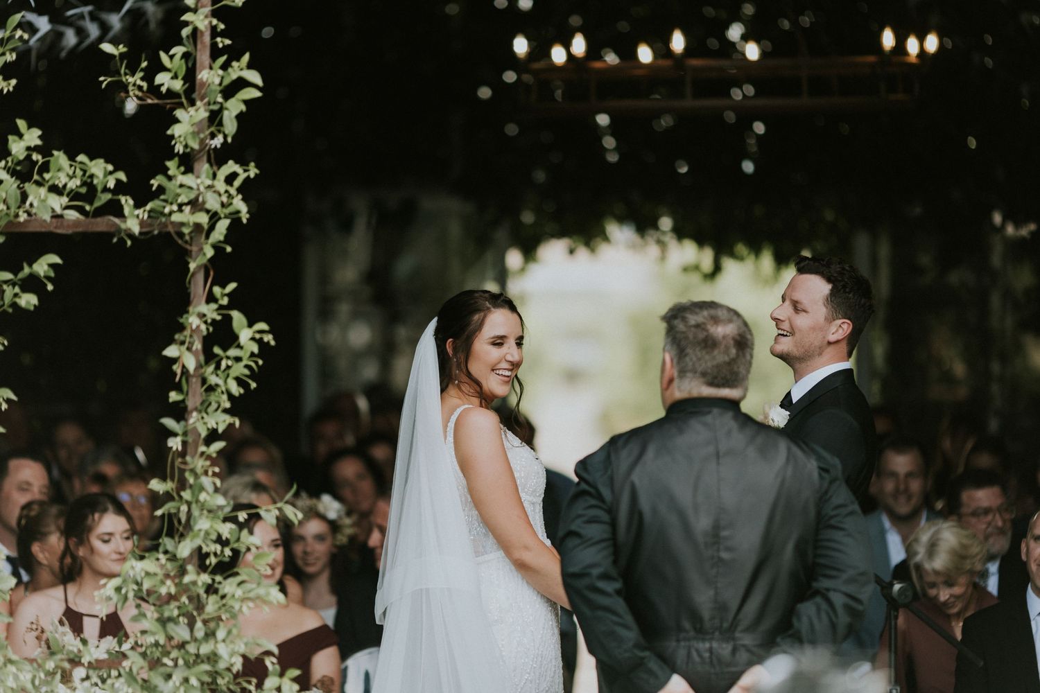 Bride and groom smiling at each other at altar during outdoor wedding ceremony with guests.