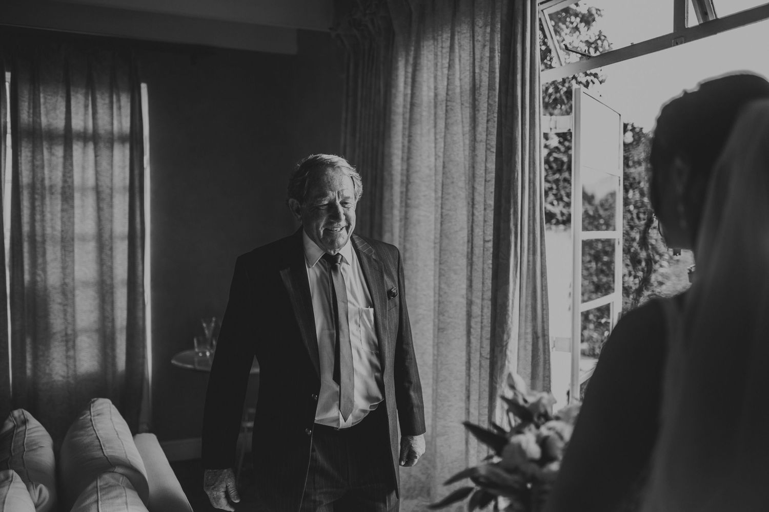 Black and white photo of older gentleman in suit approaching bride before wedding ceremony.