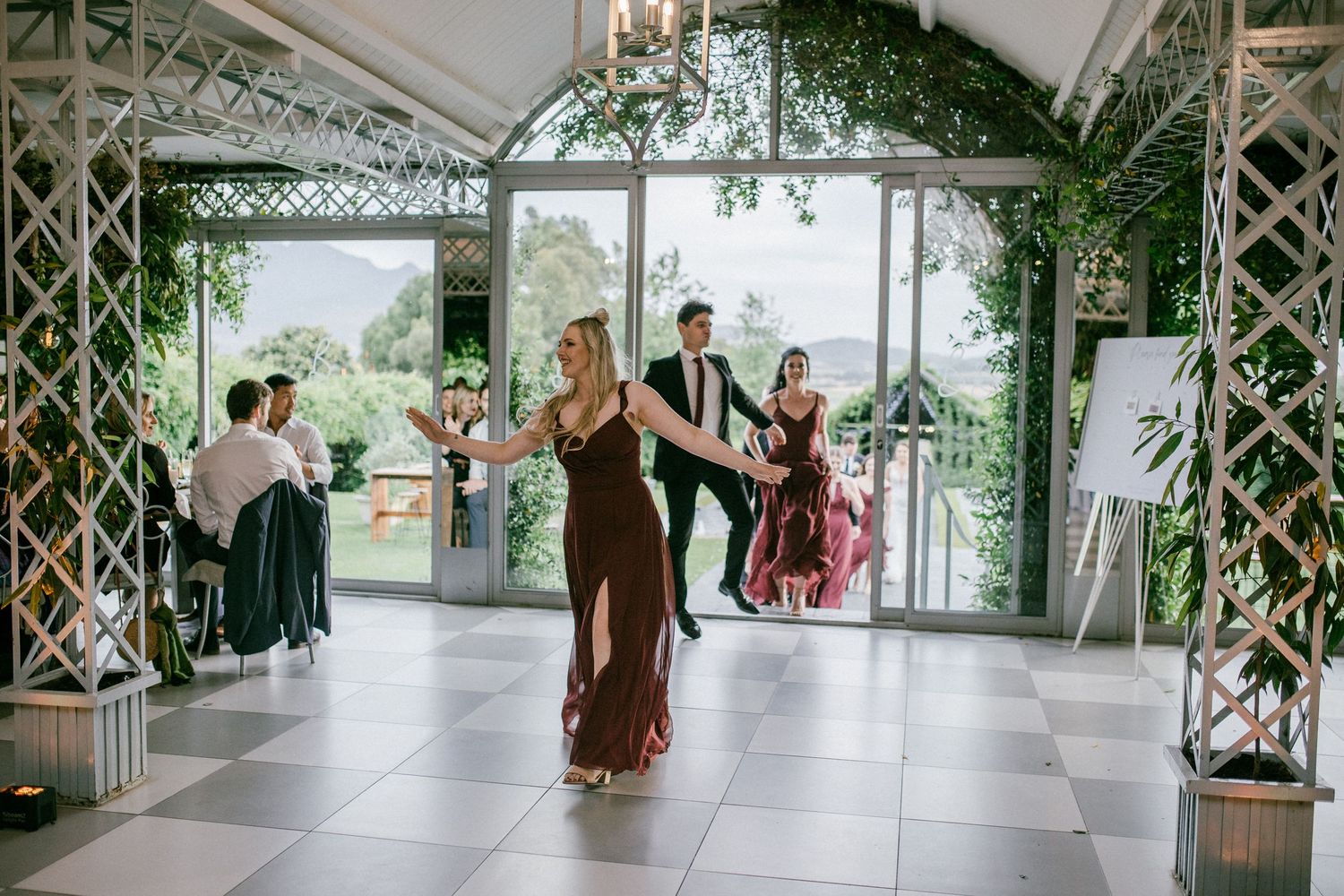 Wedding guests dancing on white dance floor under green pergola with scenic mountain views outside.
