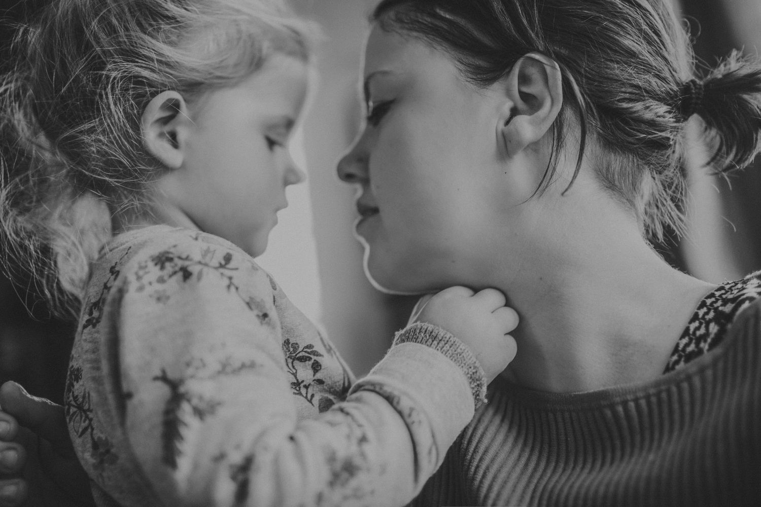 Black and white photo of a mother tenderly holding her toddler face to face in an intimate moment.