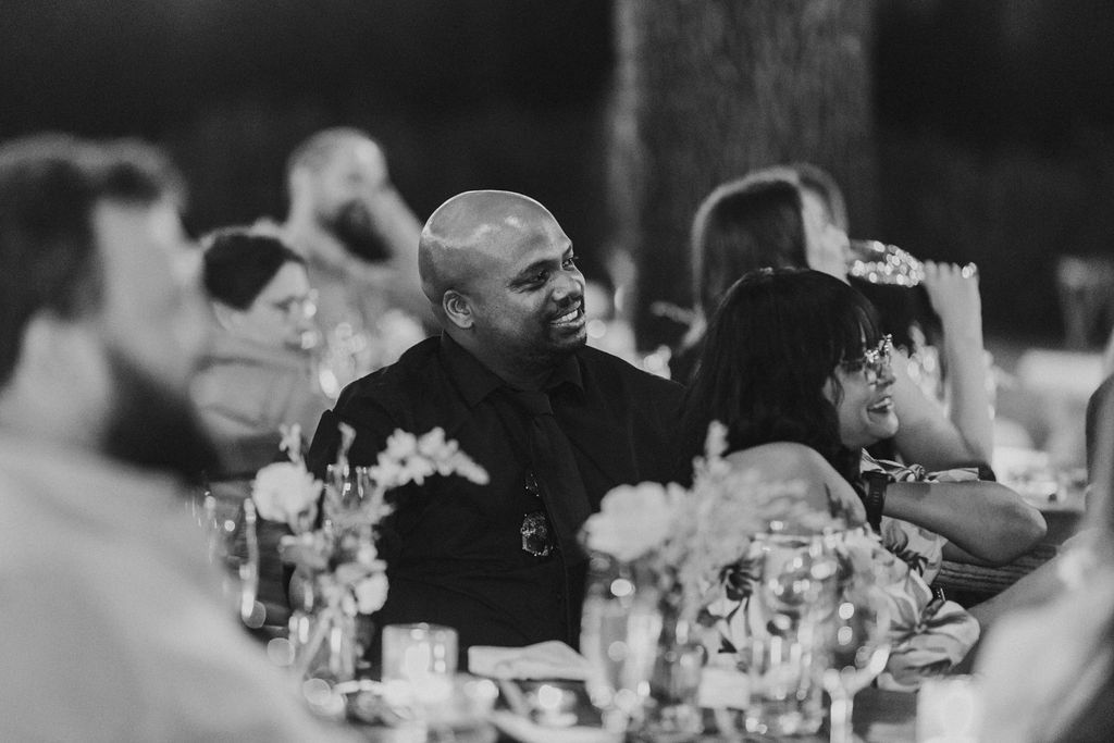Wedding guests laughing and enjoying conversation at elegantly decorated outdoor reception table.