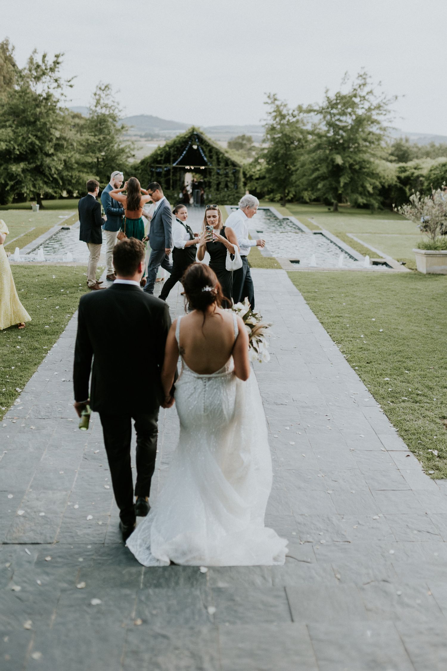 Newlyweds walking hand in hand down stone aisle past guests at a beautiful garden wedding venue.