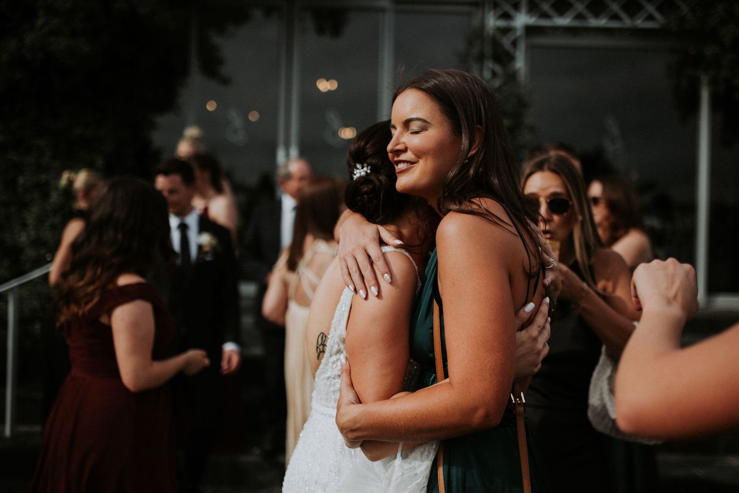 Bride shares a warm embrace with a smiling female guest during the wedding reception at an outdoor venue.
