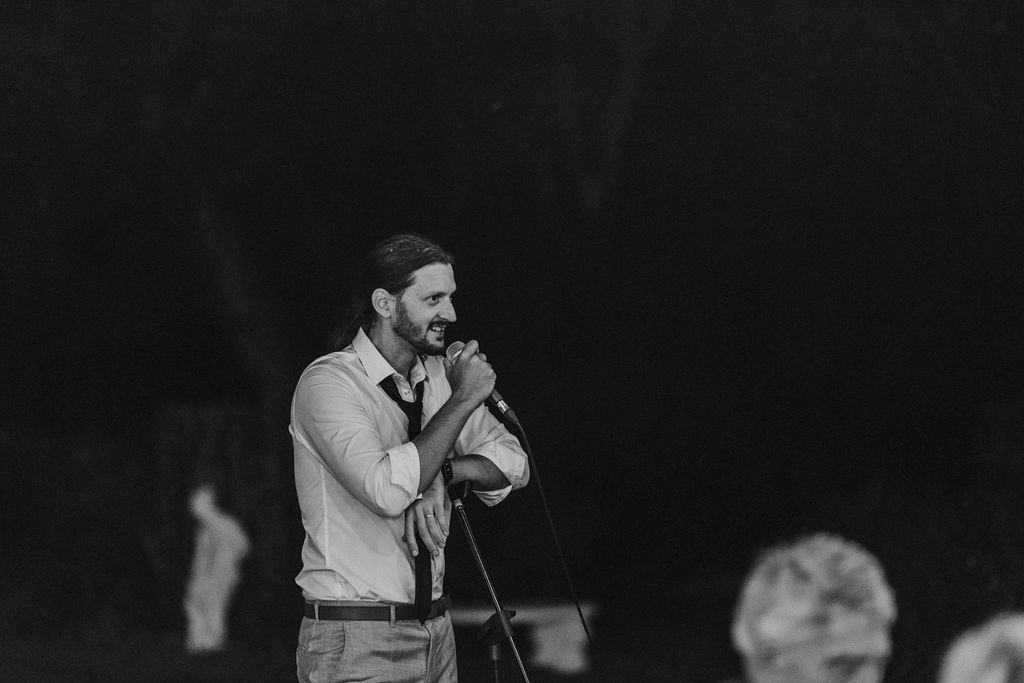Man with beard speaking into microphone at outdoor evening event in black and white photography.