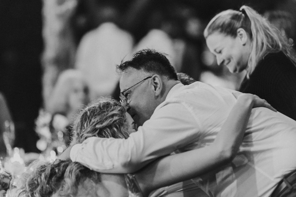 Emotional group hug between bride, groom and guest at wedding reception.