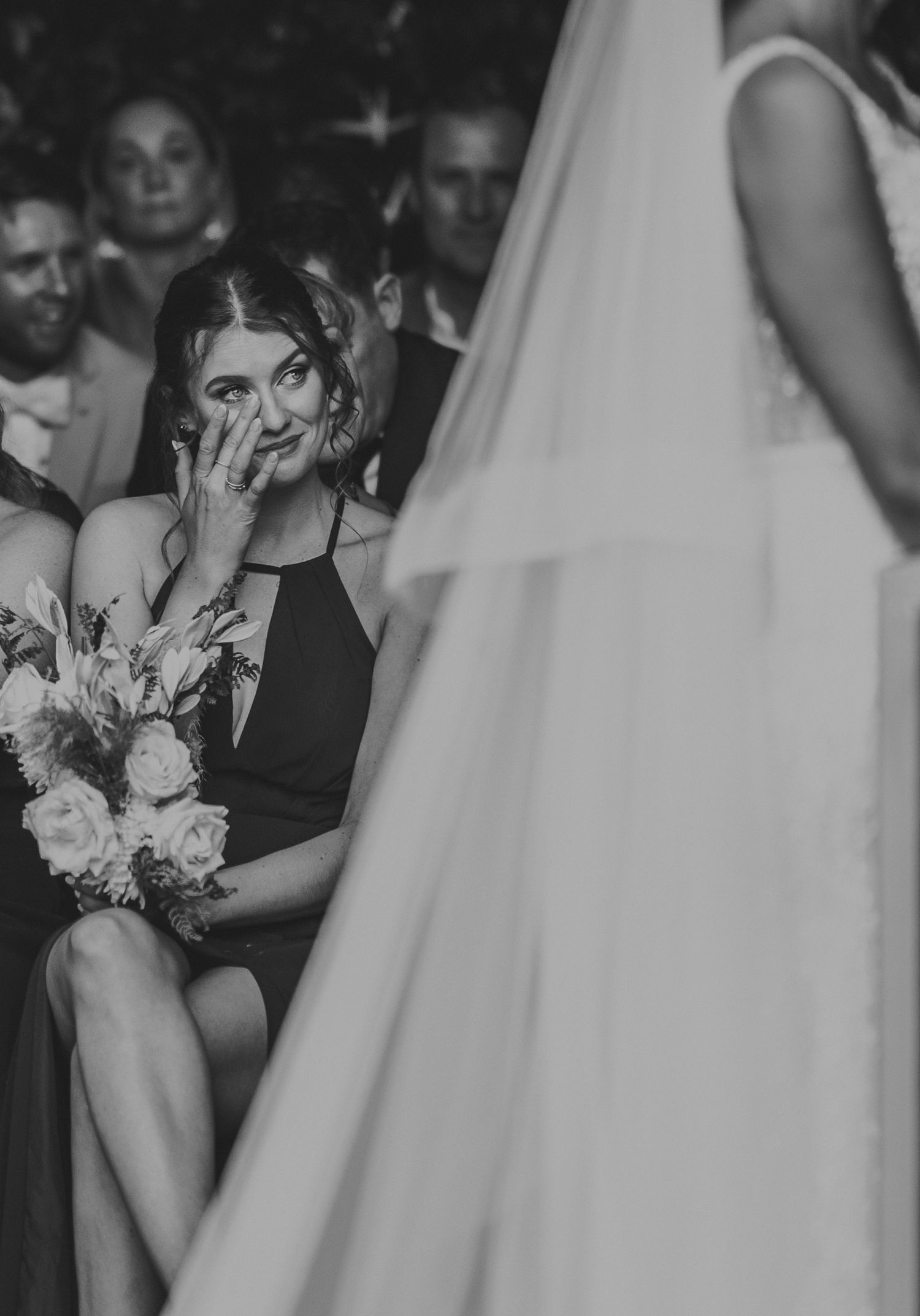 Emotional bridesmaid covers her mouth while crying during the wedding ceremony in black and white.