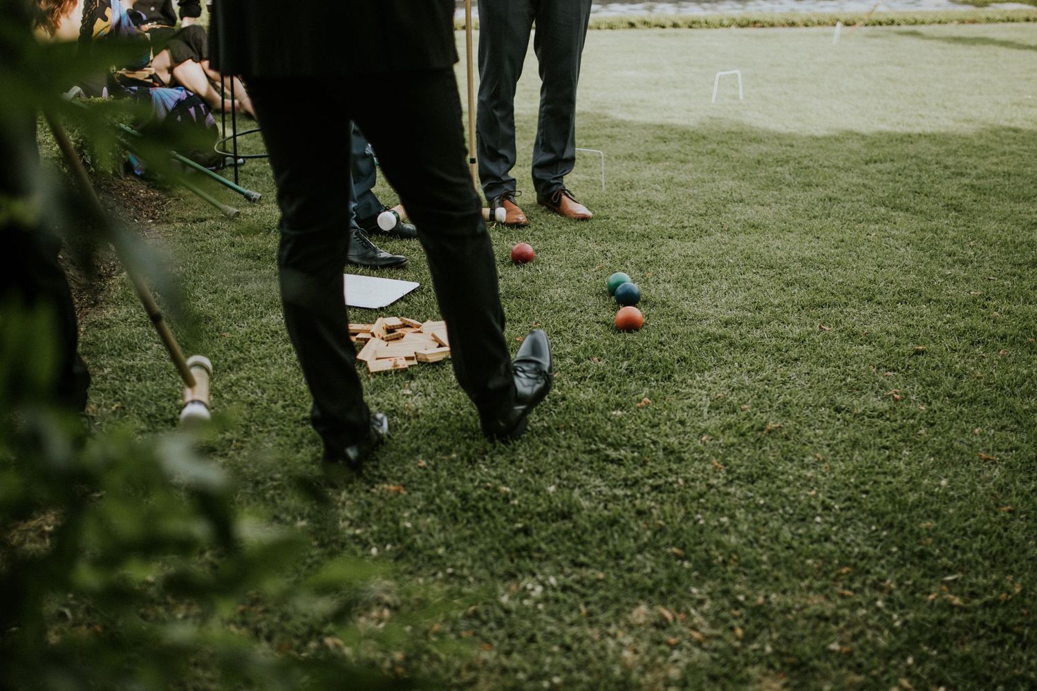 Wedding guests playing croquet on manicured grass with colorful balls during an outdoor reception.