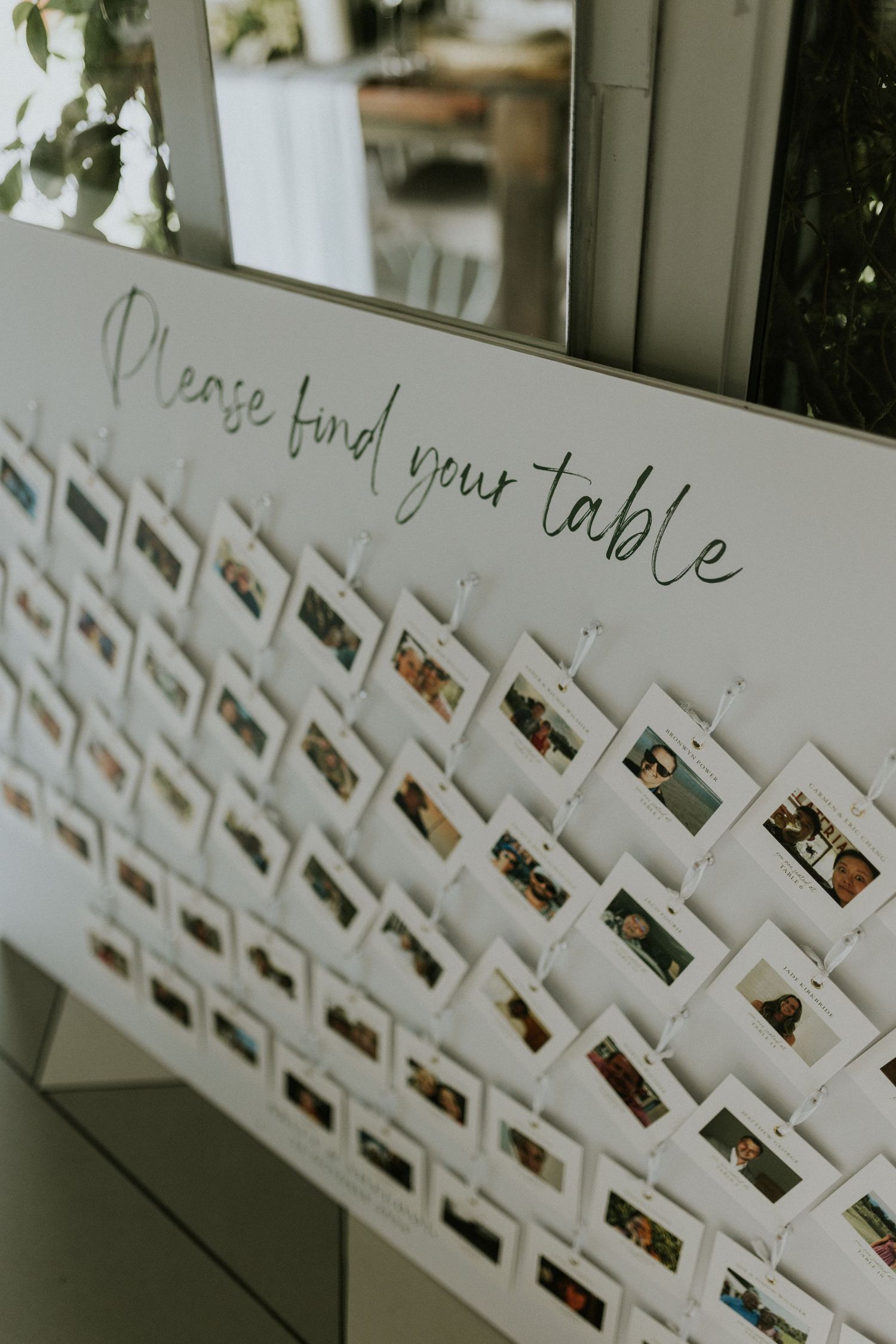Wedding seating chart display with Polaroid photos clipped to white board reading Please find your table in script font.