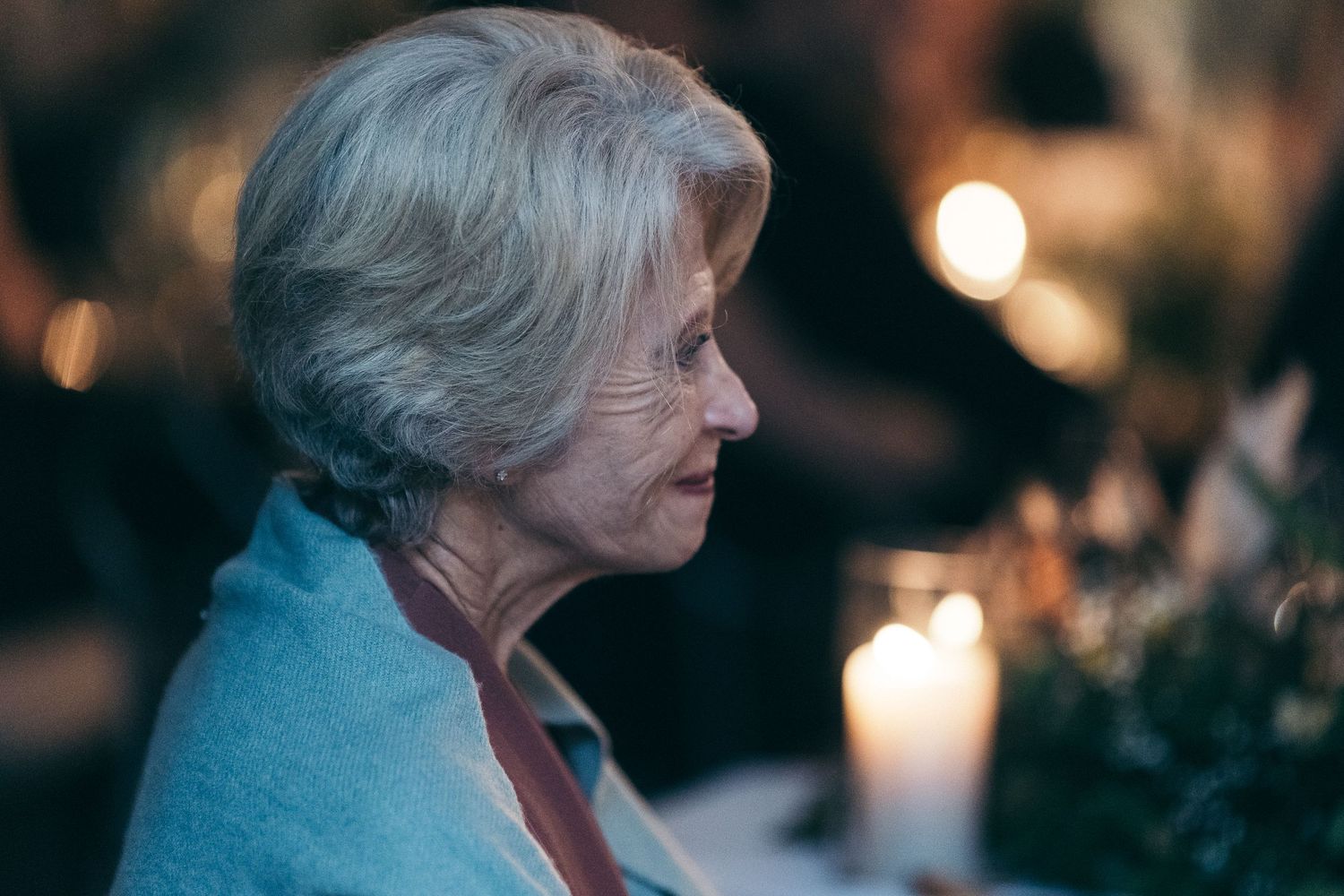 Elegant elderly woman in blue shawl seated at a candlelit wedding reception table in profile.