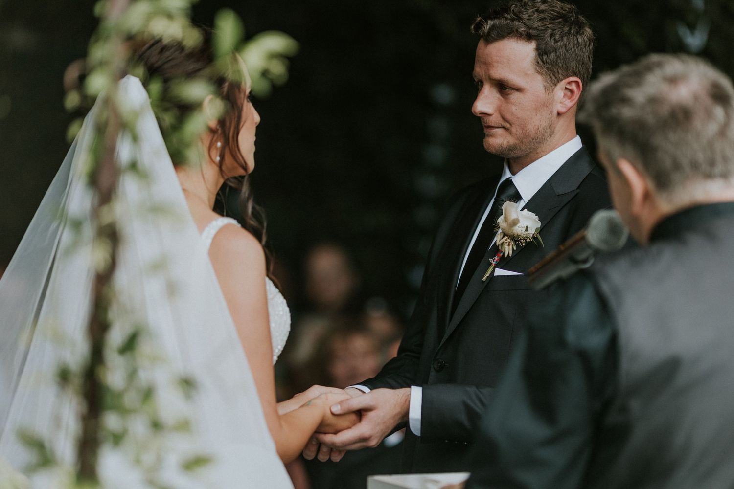 Groom gazes lovingly at his bride while holding hands during their outdoor wedding ceremony.