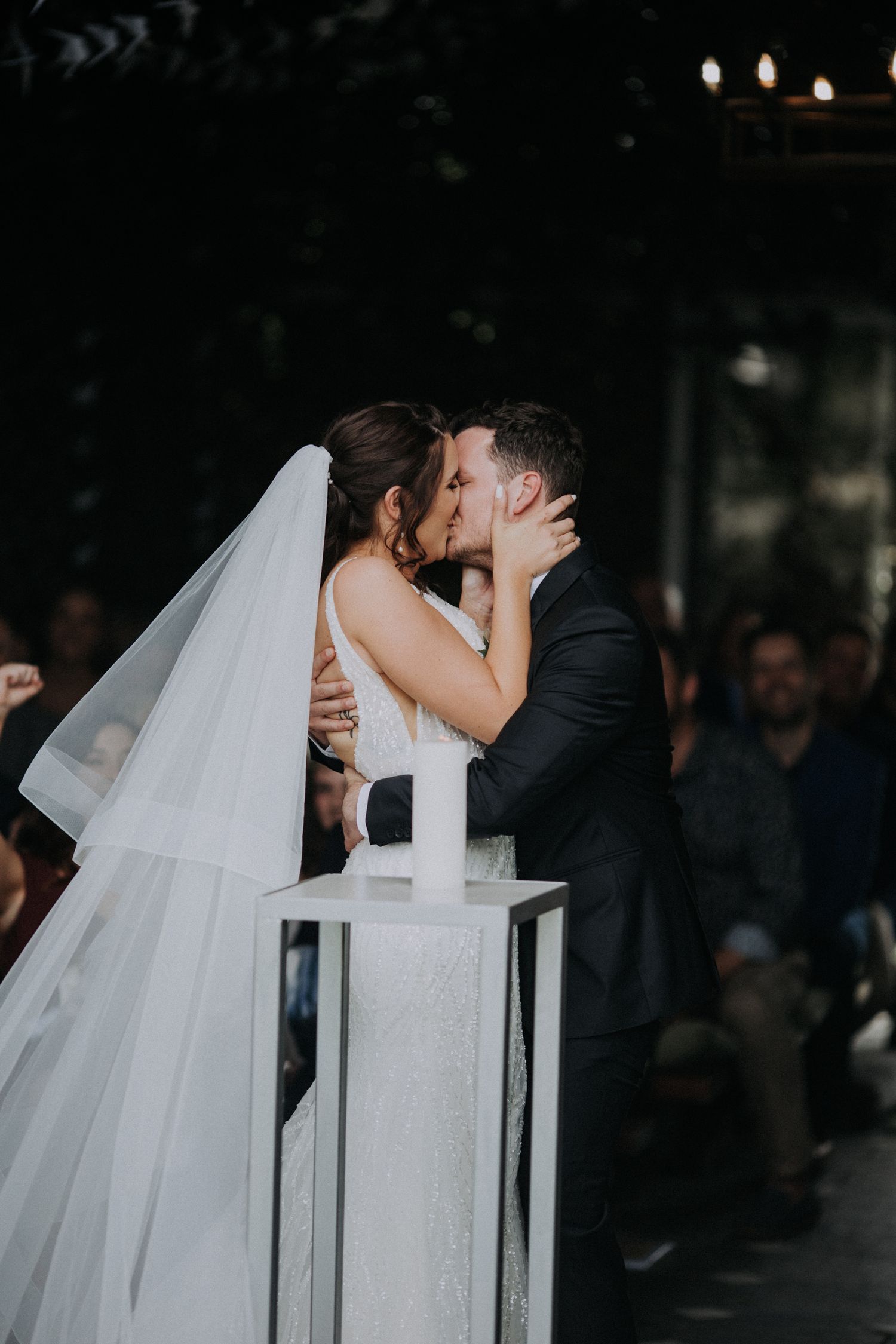 Newlyweds share their first kiss at the altar during an intimate indoor wedding ceremony with guests seated behind them.