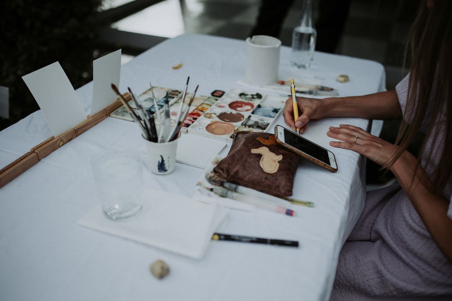 Artist painting live portraits at a white table with watercolors and brushes at a wedding reception.