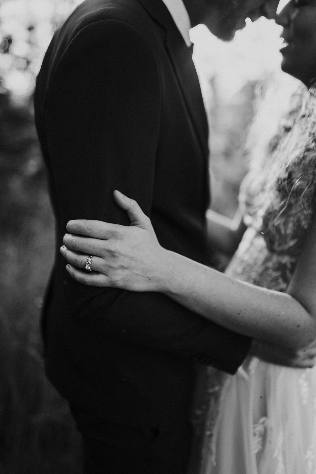 Black and white close-up of bride resting her hand on groom's arm, showcasing her elegant ring.