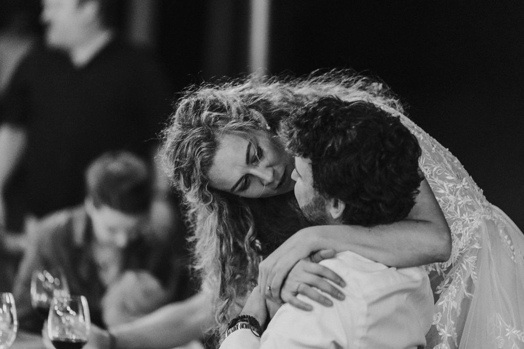 Bride embraces wedding guest warmly at outdoor evening reception dinner.