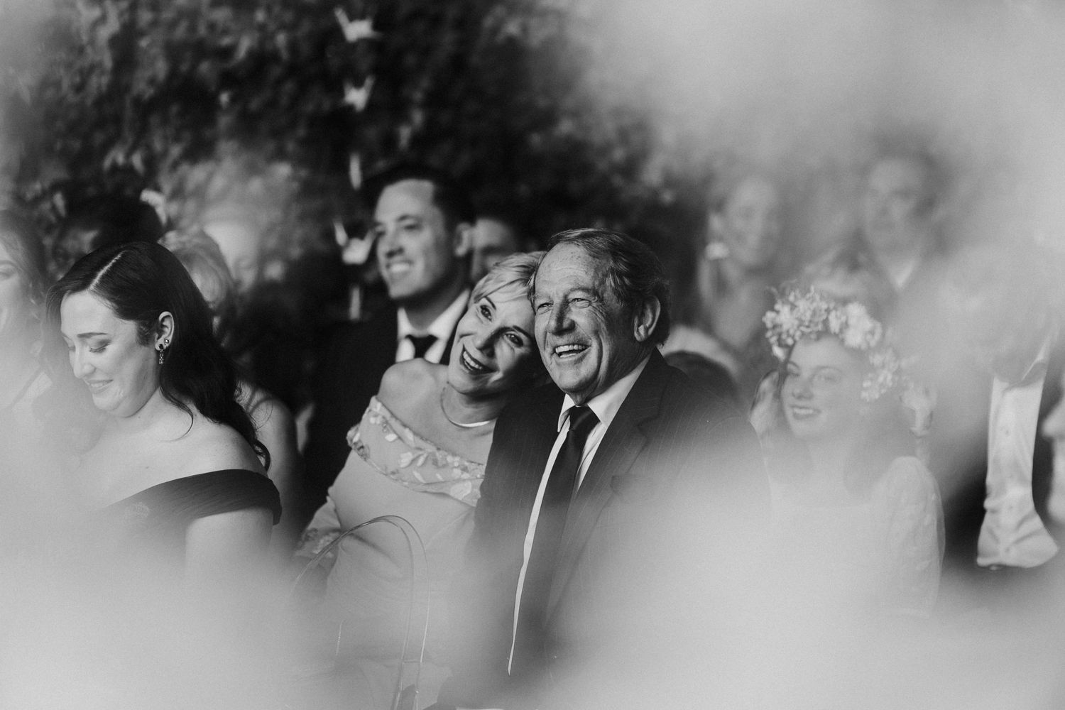 Black and white candid of smiling wedding guests enjoying emotional outdoor ceremony moments together.