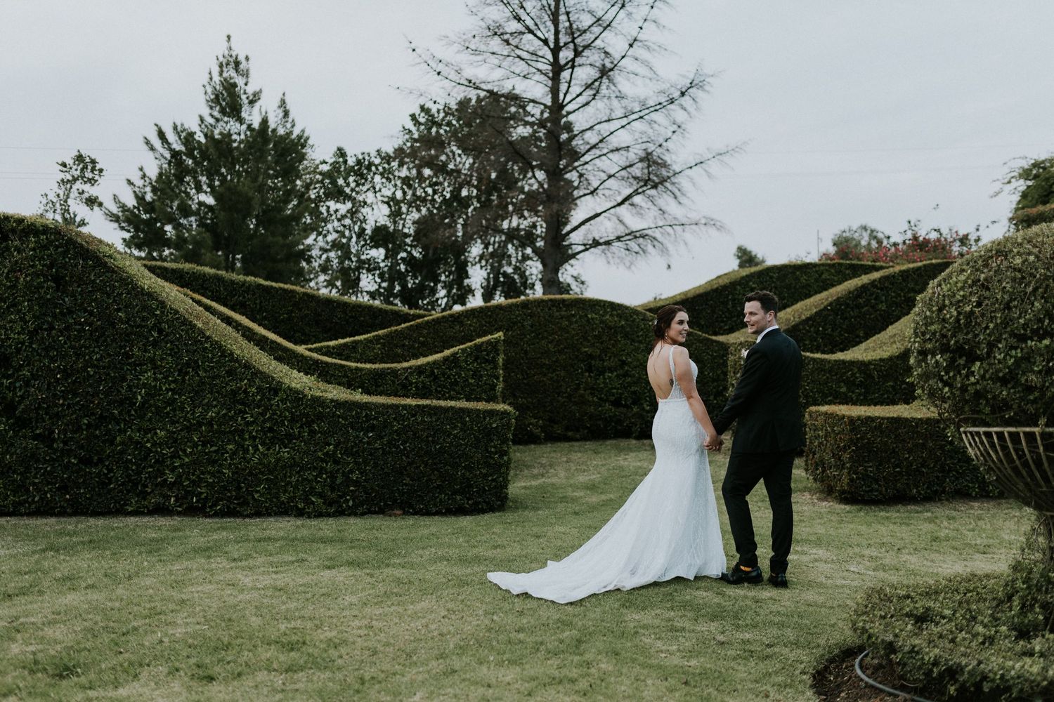 Bride and groom posing in front of sculpted hedge maze in an elegant garden wedding setting.