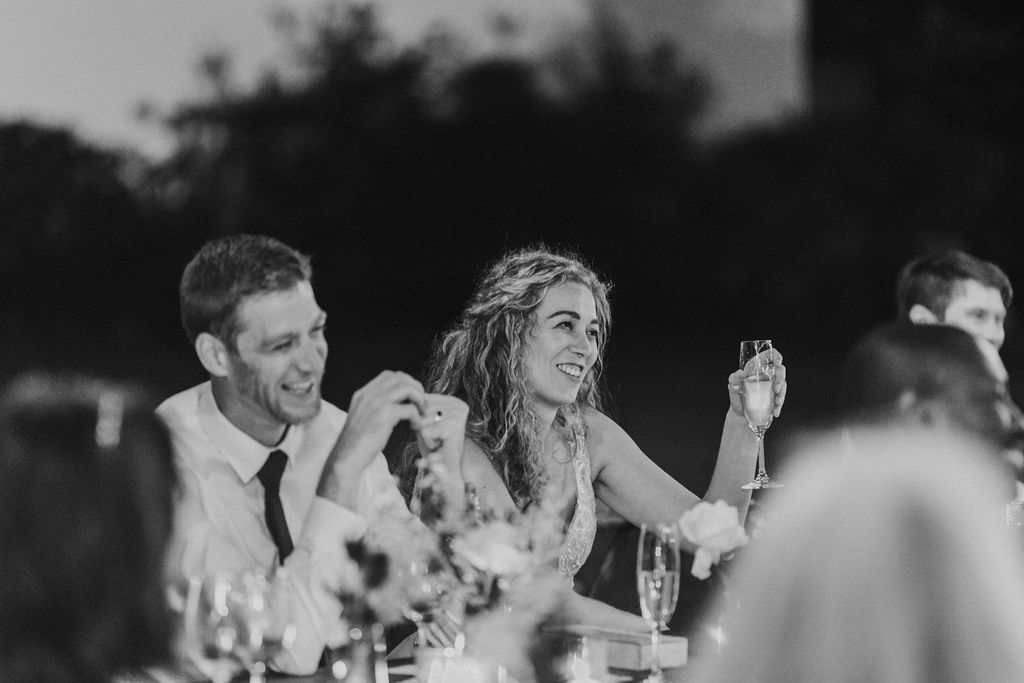 Bride and groom laugh together joyfully during outdoor wedding reception dinner speeches.