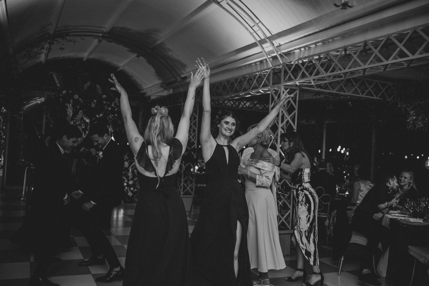 Guests dancing with arms raised at elegant wedding reception in black and white photography.