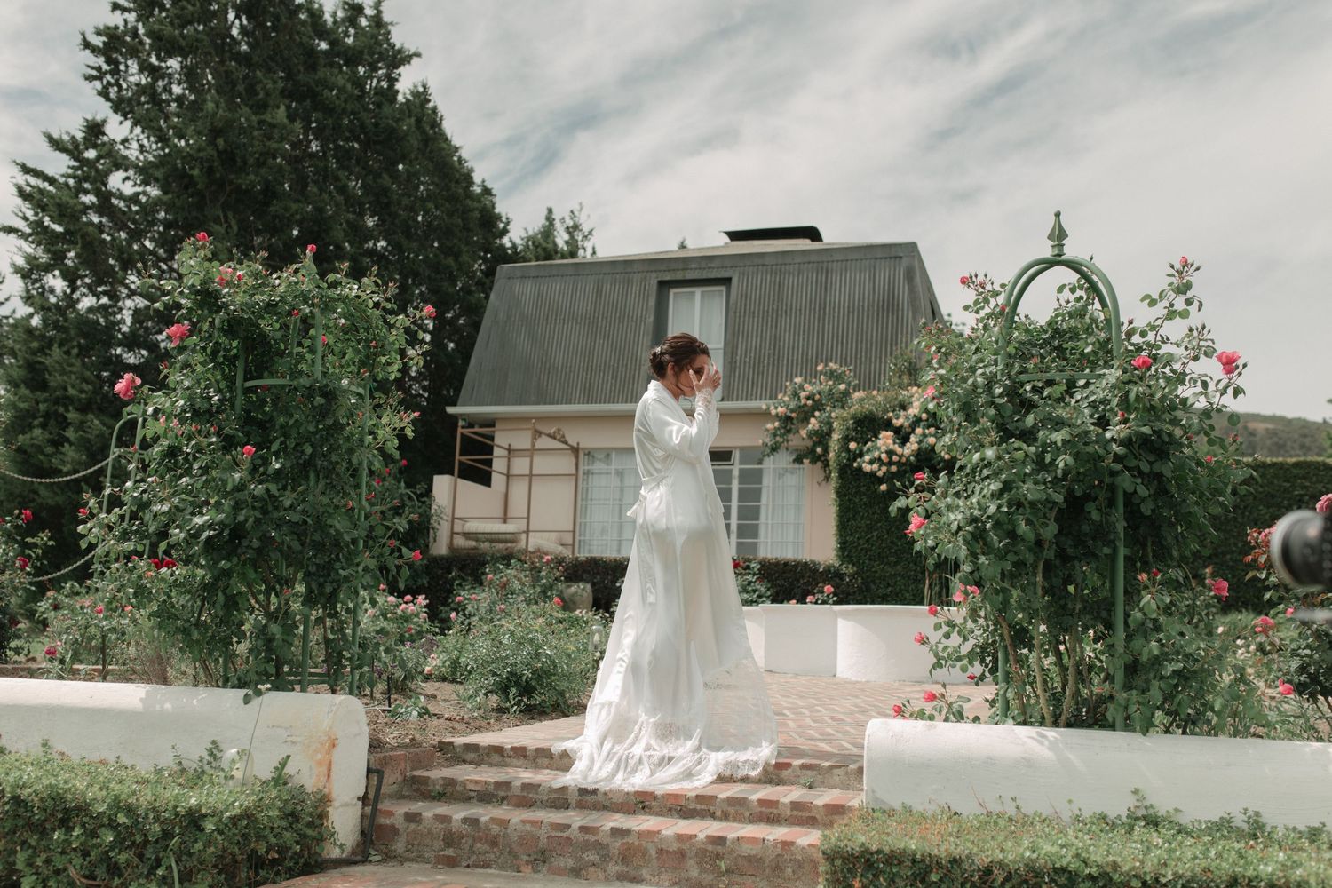 Beautiful bride in white lace wedding dress standing in rose garden outside charming venue.