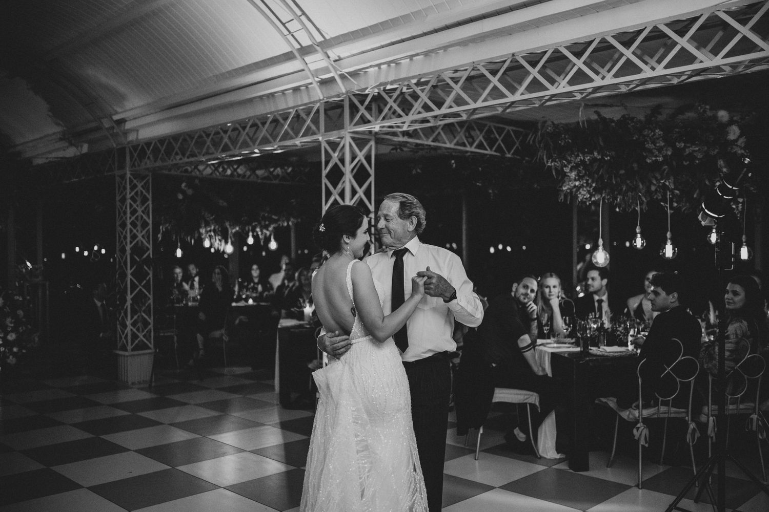 Bride and groom share first dance on checkered floor at romantic wedding reception.