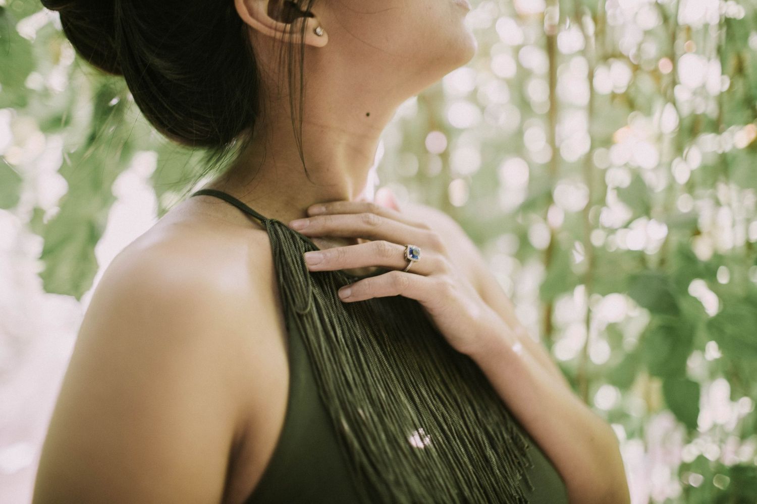 Close-up of a woman in a green dress touching her necklace surrounded by lush bokeh greenery.