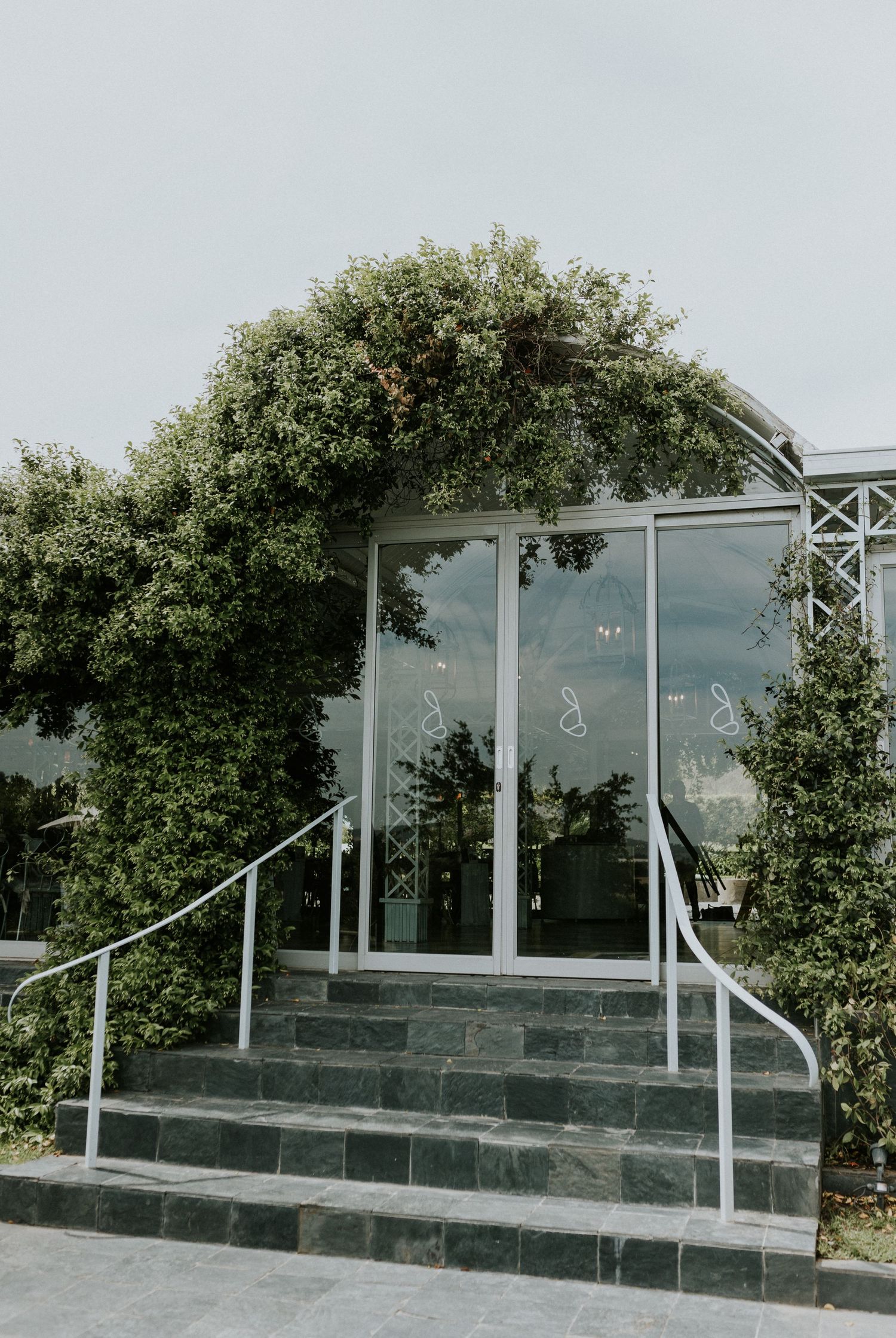 Glass entrance door framed by lush climbing green vines on a white lattice wedding venue exterior with stone steps.