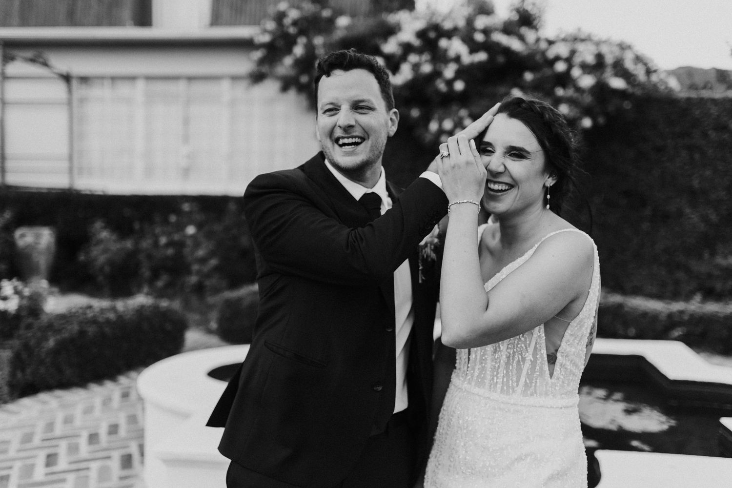 Laughing bride and groom sharing a joyful moment outdoors in black and white wedding portrait.