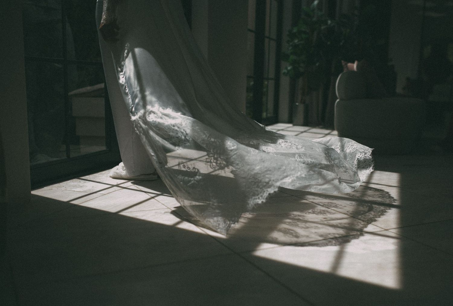 Dramatic sunlight casts shadows on elegant lace wedding dress train on floor.